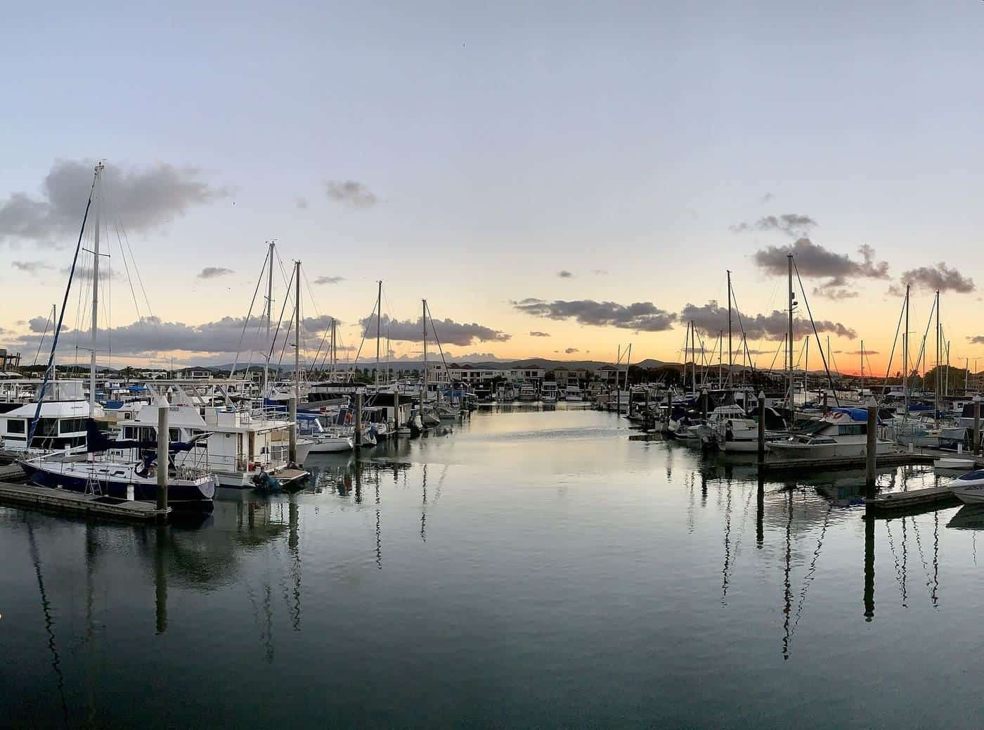 A calm marina at sunset with rows of yachts tied to pontoons